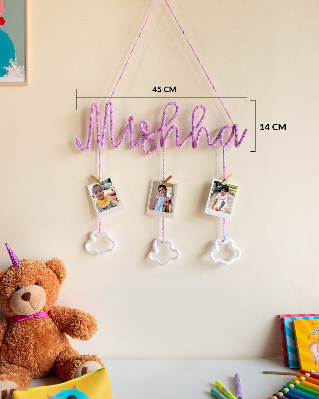 Crochet name wall hanger ‘Mishha’ with three Polaroid photos and cloud charms, measuring 45 cm wide and 14 cm tall